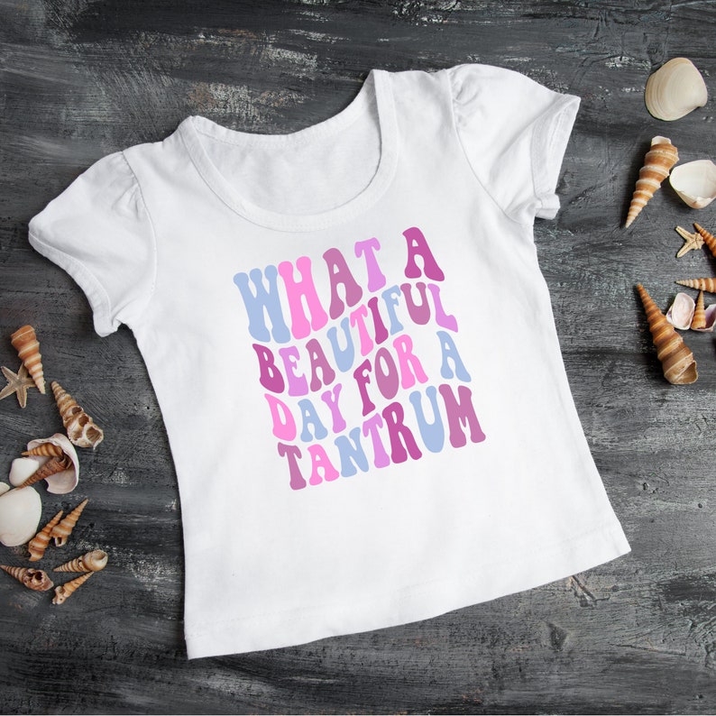 May include: White t-shirt with the text "WHAT A BEAUTIFUL DAY FOR A TANTRUM" in pink, purple, and blue letters.