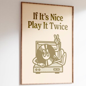 May include: A framed print with a beige background and gold text that reads "If It's Nice Play It Twice". A cartoon illustration of a record player with a record in the shape of a face with a peace sign is shown below the text.