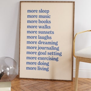 May include: A beige framed print with blue text that reads "more sleep, more music, more books, more walks, more sunsets, more laughs, more dreaming, more journaling, more goal setting, more exercising, more doing, more living."