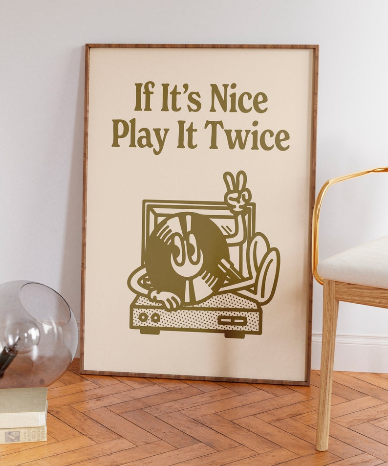 May include: A framed print with a beige background and gold text that reads "If It's Nice Play It Twice". A cartoon illustration of a record player with a record that has a face and is giving the peace sign is in the center of the print.