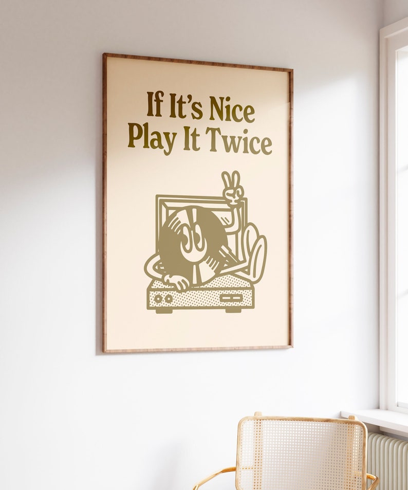 May include: A framed print with a beige background and gold text that reads "If It's Nice Play It Twice". A cartoon illustration of a record player with a record in the shape of a face with a peace sign is shown below the text.