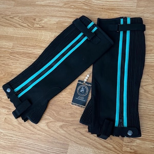 May include: A pair of black riding half chaps with turquoise stripes and zippers. The chaps have a textured design and adjustable straps. A small tag with a logo is visible.