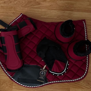 May include: A complete equestrian set in burgundy and black, including a quilted saddle pad, leg wraps, bell boots, and gloves. The set features a diamond-stitched pattern with white trim and black accents. The gloves have a black mesh design.