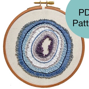 May include: A PDF pattern for a circular embroidery design featuring a layered, concentric circle pattern in shades of blue, purple, and white. The design resembles a geode or agate.