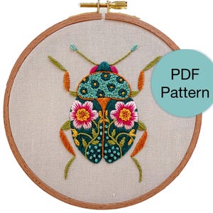 Puede incluir: Diseño de insecto bordado en un bastidor de madera. El insecto presenta bordados en color turquesa, naranja, rosa y verde. El texto "PDF Pattern" está en un círculo turquesa en la imagen. El bastidor es de madera y tiene un cierre metálico.