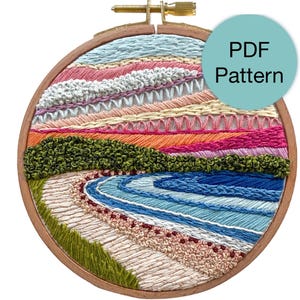 Può includere: Un'opera d'arte ricamata a mano e colorata. Il design presenta trame e colori stratificati, tra cui blu, verde, arancione, rosa e bianco. Il testo "PDF Pattern" è su un cerchio turchese. Il telaio in legno è visibile.