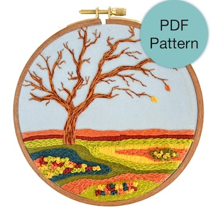 May include: An embroidered landscape scene in a wooden hoop. The design features a brown tree with bare branches against a light blue sky. The ground is a patchwork of green, orange, and yellow threads. The text "PDF Pattern" is in a blue circle.