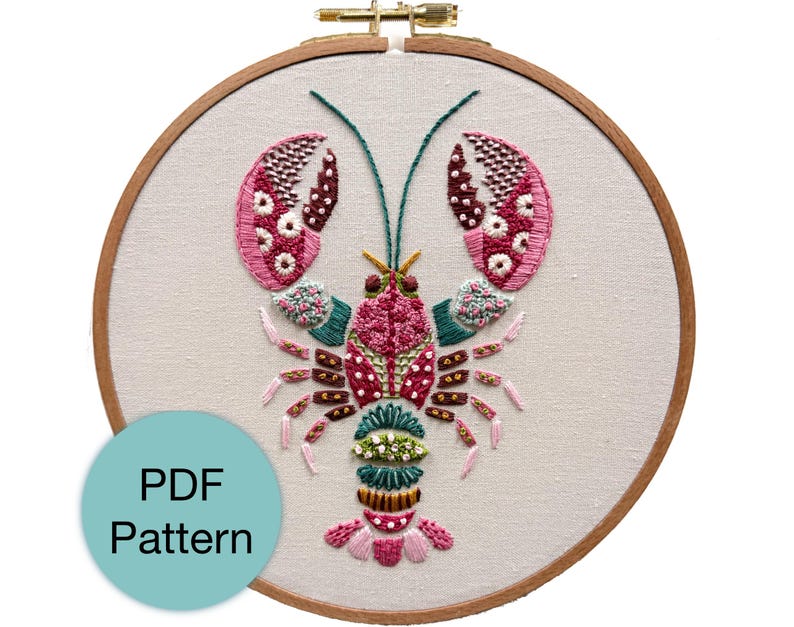 May include: Embroidered lobster design in a wooden embroidery hoop. The lobster is detailed with pink, red, green, and white thread. The text "PDF Pattern" is in a blue circle in the lower left corner.