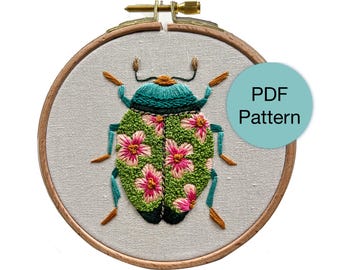 May include: Embroidered bug design in a wooden hoop. The bug features a teal head and legs, a green body with pink flower accents, and brown antennae. The text "PDF Pattern" is in a teal circle.