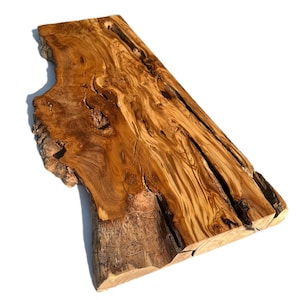 May include: A live edge wooden slab with a natural, irregular shape. The wood features a rich, warm brown color with intricate grain patterns and some cracks. The slab has a rough, unfinished edge on one side.