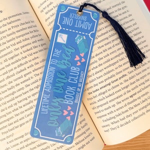 May include: A blue and pink bookmark with a keyhole design and the text "Lifetime Admission to the Only One Bed Book Club". The bookmark has a black tassel.