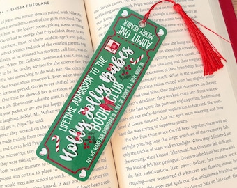 Puede incluir: Un marcapáginas verde con un borla roja. El marcapáginas tiene un tema festivo navideño con un bastón de caramelo rojo y blanco, hojas de acebo y lazos rojos. El texto en el marcapáginas dice "Admisión de por vida al Holly Jolly Babes Book Club". El texto "Todo lo que queremos para Navidad es una pila de libros y una noche acogedora" también está en el marcapáginas.