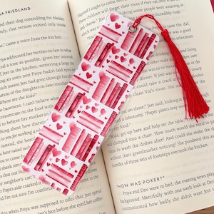 May include: A bookmark with a red and white design featuring stacks of books and hearts. The bookmark has a red tassel.