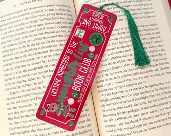 Puede incluir: Un marcapáginas rojo y verde con un diseño de hombre de jengibre. El marcapáginas tiene forma de billete y tiene el texto "Lifetime Admission to the Mangoty List Book Club".