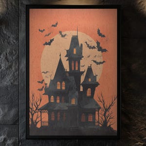 May include: A framed print with a Halloween theme, showing a silhouette of a haunted house against a peach-coloured backdrop with a full moon. Bats fly in the sky. The print is in a black frame.