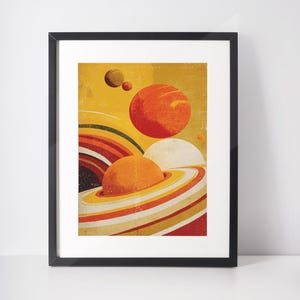 May include: Framed art print featuring a retro-style illustration of planets and rings in shades of orange, yellow, and red against a yellow background. The artwork has a vintage, textured appearance, with a black frame.