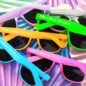 Pode incluir: Um conjunto de seis óculos de sol coloridos com lentes pretas. Cada par tem o texto "Ben & Shaun 11.07.2023" impresso nas hastes.