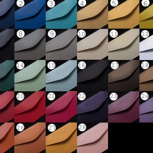 Op de afbeelding: Een raster van achtentwintig genummerde kleurstalen met diverse tinten leer of stof, waaronder blauw, groen, grijs, bruin, rood, paars en roze. Elke staal heeft een gevouwen envelopklep tegen een zwarte achtergrond.