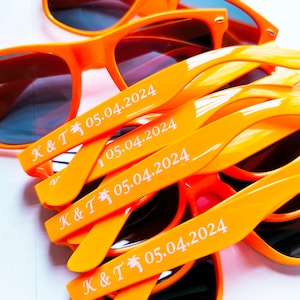 May include: A stack of orange plastic sunglasses with the text "K & T 05.04.2024" printed on the arms.