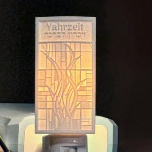 May include: A white night light with a clear plastic insert featuring a tree design and the text "Yahrzeit" and Hebrew text. The night light has an on/off switch.