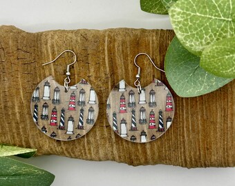 May include: A pair of round, clear acrylic earrings with a lighthouse pattern. The earrings are silver and have a hook closure.