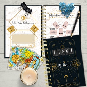 May include: A black and gold tarot journal with the words "Tarot Mi Diario" and "Wheel of Fortune" on the cover. The journal has a gold spiral binding and is open to a page with a tarot spread and questions about personality, relationships, and strength.