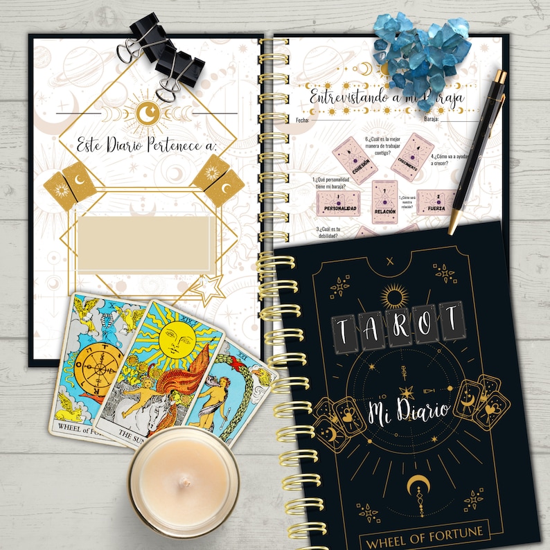 May include: A black and gold tarot journal with the words "Tarot Mi Diario" and "Wheel of Fortune" on the cover. The journal has a gold spiral binding and is open to a page with a tarot spread and questions about personality, relationships, and strength.