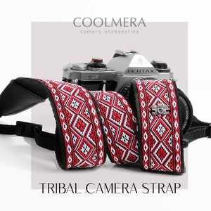 May include: Red and white tribal patterned camera strap with black adjustable straps and a silver camera strap connector. The strap is attached to a silver Pentax camera. COOLMERA camera accessories. TRIBAL CAMERA STRAP