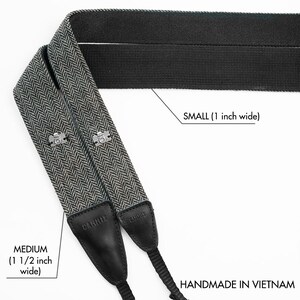 May include: Two camera straps, one black and one black and white herringbone pattern. The black strap is 1 inch wide and the herringbone strap is 1 1/2 inches wide. Both straps are labeled "CANNIX" and say "HANDMADE IN VIETNAM".