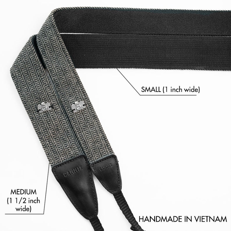 May include: Two camera straps, one black and one black and white herringbone pattern. The black strap is 1 inch wide and the herringbone strap is 1 1/2 inches wide. Both straps are labeled "CANNIX" and say "HANDMADE IN VIETNAM".