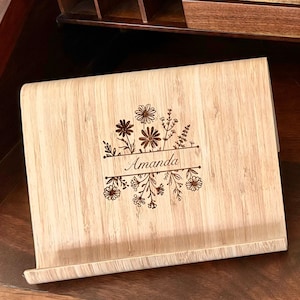 May include: A light brown bamboo book stand with a floral design and the name "Amanda" engraved on it.