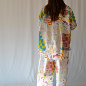 Puede incluir: Una camisa blanca de botones y pantalones a juego con un estampado abstracto colorido que presenta formas geométricas, remolinos y puntos.