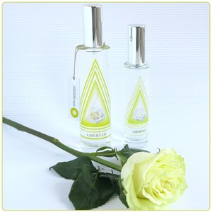 Può includere: Due bottiglie di vetro con tappi argentati ed etichette che recano la scritta "LIBERTAD" in un design a triangolo verde. Le bottiglie sono su una superficie bianca con una rosa bianca e uno stelo verde.