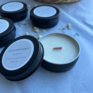 May include: A black metal tin candle with a wooden wick. The candle is labeled "South Loop Scents" and "Jasmine & Rosemary" with the text "Soy Candle | 1.25 oz".