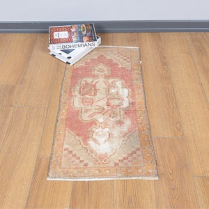 May include: A vintage Turkish runner rug with a faded red, beige and white geometric pattern. The rug is approximately 60 cm by 150 cm.
