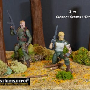 Op de afbeelding: Een aangepaste decor set voor 1:12 schaal diorama's. Twee actiefiguren in militaire kleding staan in een bosrijke omgeving met bomen, mos en gevallen bladeren. De tekst "3 PC CUSTOM SCENERY SET" is zichtbaar.