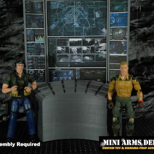 Pode incluir: Uma cena de diorama com duas figuras de ação em frente a um painel de controle com várias telas exibindo mapas e dados. As figuras estão vestidas com roupas de estilo militar. A cena é ambientada em um fundo rochoso. O texto na parte inferior diz "MINI ARMS DEPOT".