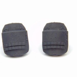 Op de afbeelding: Twee zwarte rubberen bumpers met een rechthoekige vorm en een getextureerd oppervlak. Elke bumper heeft een gebogen bovenkant en drie horizontale ribbels. Ontworpen voor impactbescherming.
