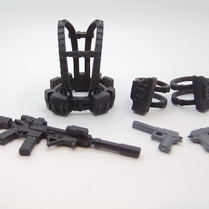 May include: A collection of black toy tactical gear, including a vest, holsters, and various firearms. The set includes a rifle and two pistols, all in a matte black finish. The items are arranged on a white surface.