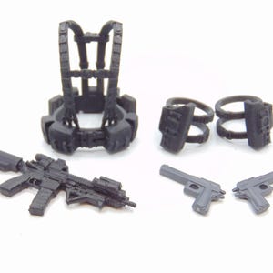 Op de afbeelding: Een verzameling miniatuur zwart speelgoed militaire accessoires, waaronder een tactisch vest, twee pistoolhouders, twee pistolen en een aanvalsgeweer. De items zijn gerangschikt op een wit oppervlak.