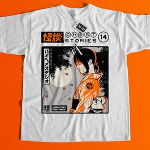 Op de afbeelding: Wit T-shirt met een zwarte en oranje grafische print van een vrouw met hoorns en Japanse tekst. De tekst luidt "Ghost Stories" en "14".