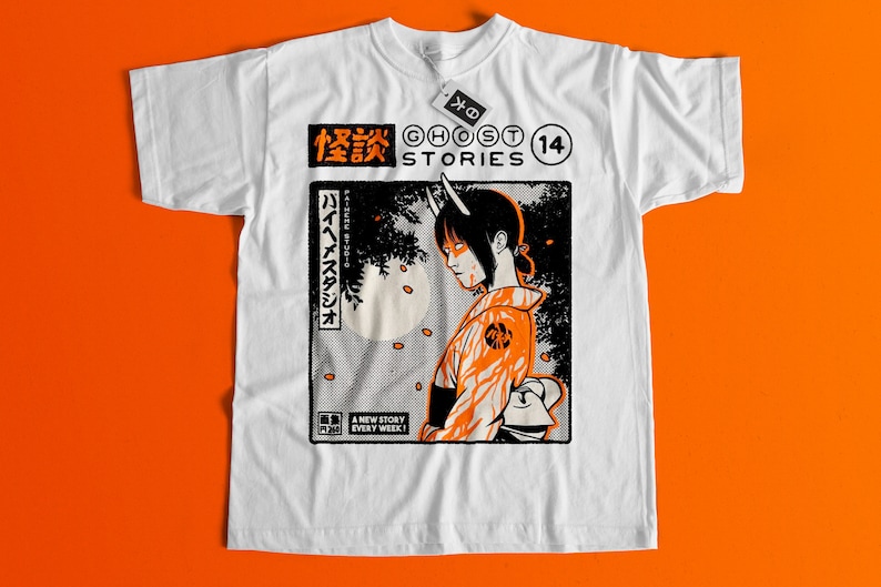 Op de afbeelding: Wit T-shirt met een zwarte en oranje grafische print van een vrouw met hoorns en Japanse tekst. De tekst luidt "Ghost Stories" en "14".