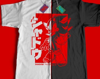 Può includere: Una t-shirt bianca e nera con una grafica rossa e bianca di Shadow the Hedgehog della serie di videogiochi Sonic the Hedgehog. La grafica include il testo giapponese "シャドウ" che significa "Shadow" in inglese. Il testo "SHADOW - シャドウ" è incluso anche nella grafica.