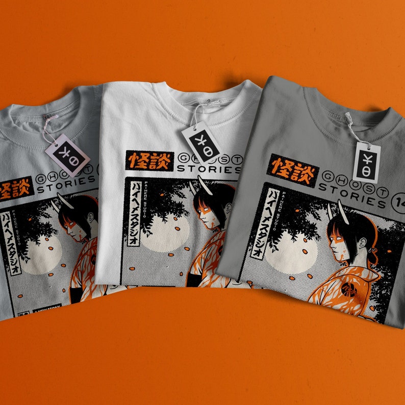 Op de afbeelding: Drie grijze, witte en lichtgrijze T-shirts met een grafische print van een vrouw met hoorns en Japanse tekst die "怪談" leest, wat "Spookverhalen" betekent.