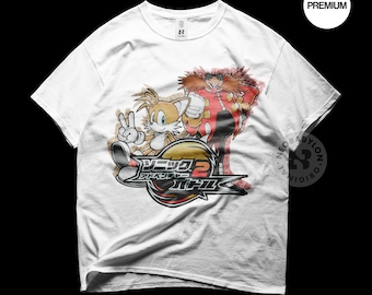 May include: White t-shirt with a graphic print of Tails and Dr. Eggman from the Sonic the Hedgehog video game series. The graphic is in a distressed style and includes the text "ソニック アドベンチャー 2 バトル".