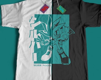 Può includere: Una t-shirt bianca e nera con una grafica turchese di Silver the Hedgehog della serie di videogiochi Sonic the Hedgehog. La grafica include il testo giapponese "SILVER - ヘッジホッグ".