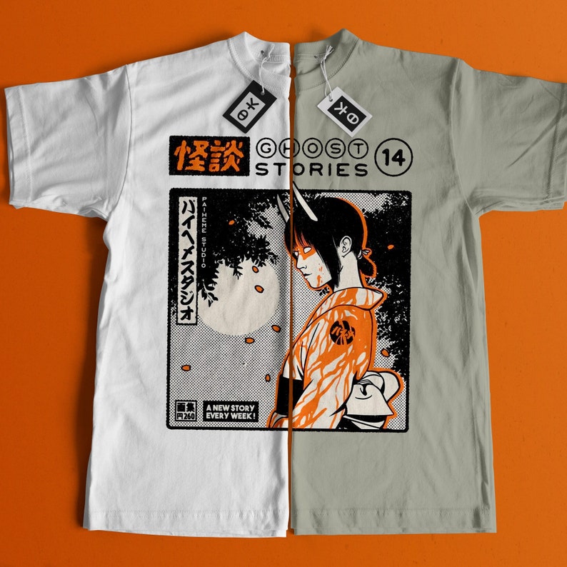 Op de afbeelding: Een wit en grijs t-shirt met een gesplitst ontwerp. De linkerzijde toont een Japanse manga-stijl illustratie van een vrouw met hoorns en een rood-oranje outfit. De rechterzijde toont de tekst "Ghost Stories" en "14" in een zwart-wit lettertype. De tekst "バイヘメスタジオ" is ook zichtbaar in het Japans.