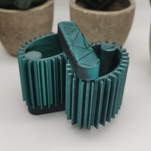 May include: A teal green 3D printed box with a gear-like design. The box is open and has a smaller teal green piece inside.