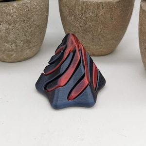 Pode incluir: Uma pirâmide geométrica impressa em 3D com um esquema de cores vermelho e azul. A pirâmide tem uma superfície texturizada e um ponto afiado no topo.