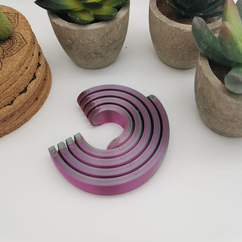 Puede incluir: Un conjunto de seis anillos met&aacute;licos encajables en un degradado arco&iacute;ris de morado y verde. Los anillos est&aacute;n apilados en forma de semic&iacute;rculo.